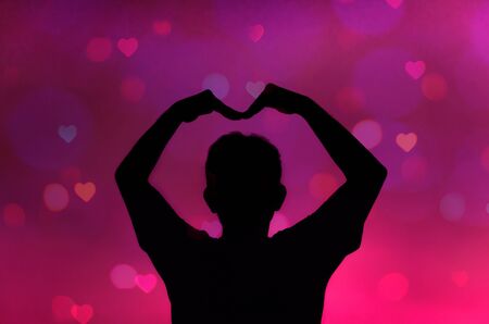 Silhouette of man making heart shape on pink background with heart bokehの写真素材