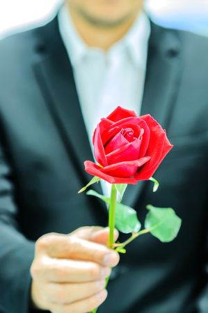 A man is giving red rose. Photo is focused at the rose.の写真素材