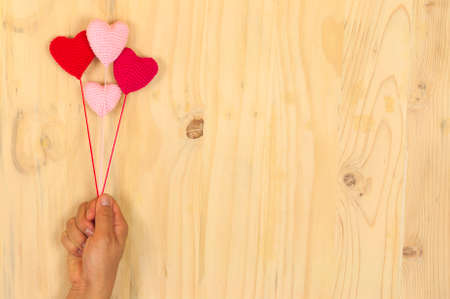 Hand holding floating red and pink crochet heart over wooden backgroundの写真素材
