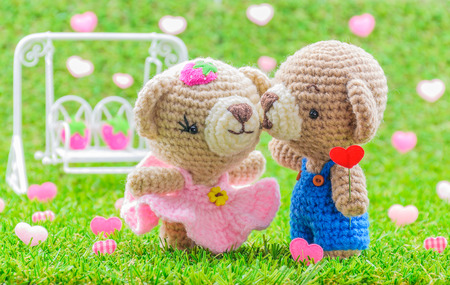 Lovely kiss baby bears crochet doll on green grass with blurred swing and heart background.の写真素材