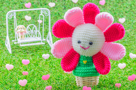 Happy baby blooming flower crochet doll on green grass with blurred pink heart and white swing decoration.の写真素材