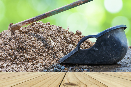 White wooden terrace with hoe and clam-shell shaped bucket and soil mound over green bokeh backgroundの写真素材
