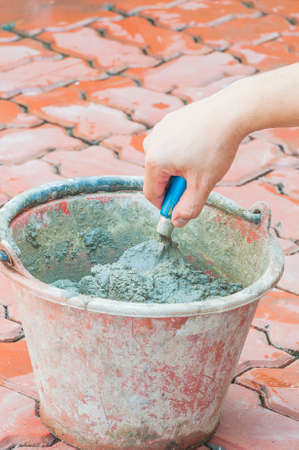 Hand holding trowel mixing mortar in a bucketの写真素材