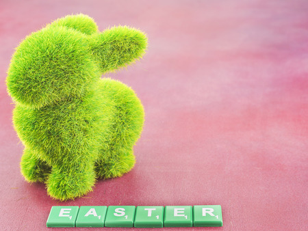 Artificial green grass rabbit and Easter word over pink background