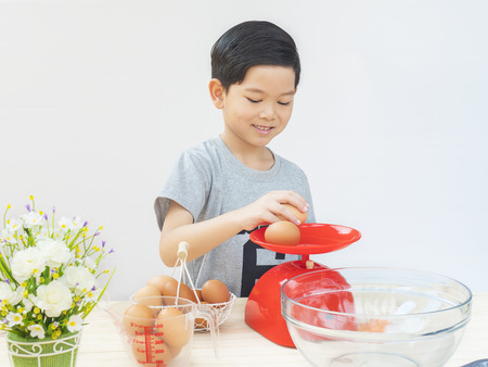 A boy is weighing raw eggs preparing to make a cake.の写真素材