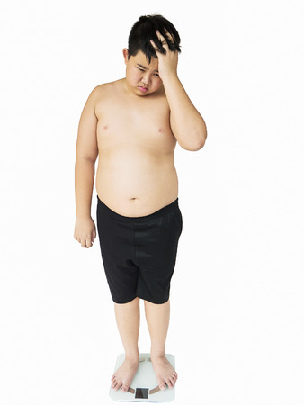 Soft focus of fat boy disappoint his fatness while standing on on weighing machine over white backgroundの写真素材