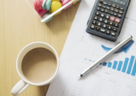 Business financial working concept, pen an calculator on growth bar graph with coffee cup and macaroon background selective focusedの写真素材