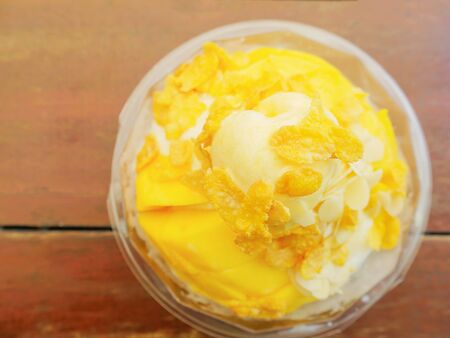 Top view of snow ice cream with mango and cornflakes topping on wooden tableの写真素材