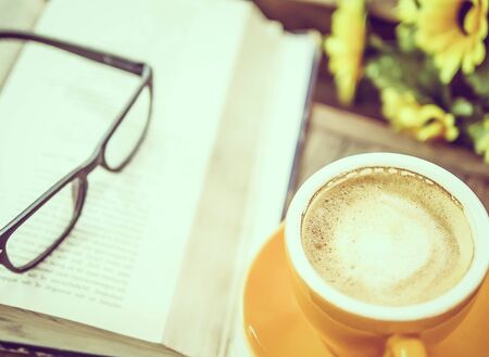 Vintage photo of a cup of coffee with book and reading glasses on wooden table, selective focusedの写真素材
