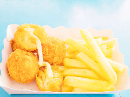French fries and fried cheese balls in paper container over blue table backgroundの写真素材