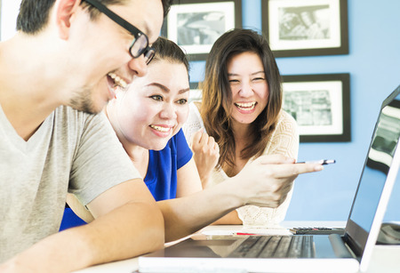 Two women and one man are happily looking at computer in modern officeの写真素材