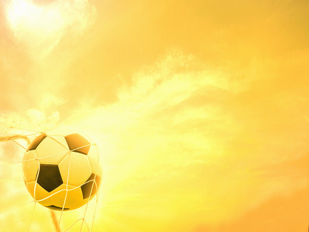 Football in goal net with warm yellow sky backgroundの写真素材