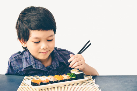 Vintage style photo of asian lovely boy is eating sushiの写真素材