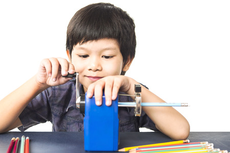 A boy is sharpening his pencil using mechanical sharpener over white backgroundの写真素材