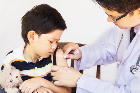 Sick Asian boy being treated by male doctor over white backgroundの写真素材