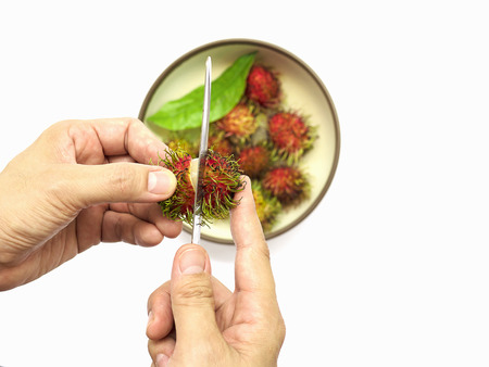 A man is peeling fresh rambutan using kitchen knife, isolated over whiteの写真素材