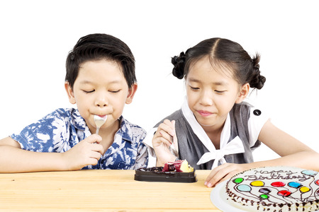 Asian kids are happily eating homemade cake over white backgroundの写真素材