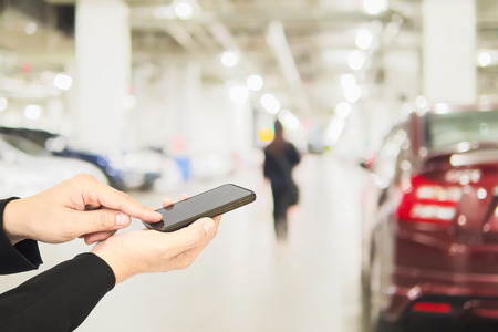 Hand is using telephone over blurred photo of a woman is walking dangerously in a car parking areaの写真素材