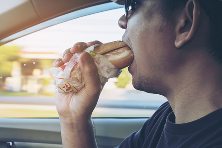Man is dangerously eating hot dog and cold drink while driving a carの写真素材