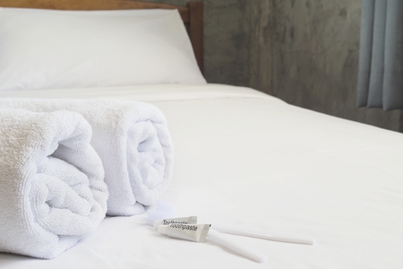 Hotel towel set with toothbrush and toothpaste on white bedの写真素材