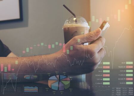 Man is using mobile phone while sitting in coffee shop checking stock data with chart and information overlayの写真素材