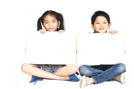 10 and 7 years Asian school girl and boy happily showing empty white book isolated over whiteの写真素材