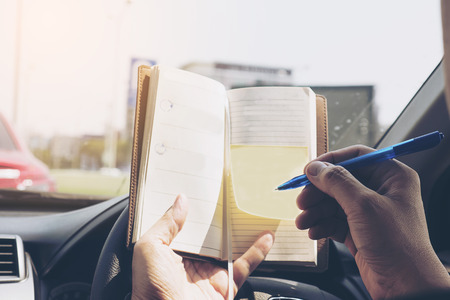 Man writing notebook while driving car, dangerous behaviorの写真素材