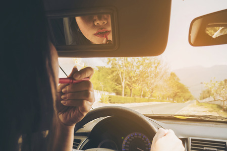 Woman making up her face using lipstick while driving car, unsafe behaviorの写真素材