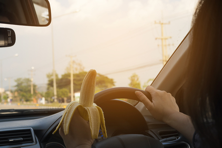 Lady eating banana while driving car dangerouslyの写真素材