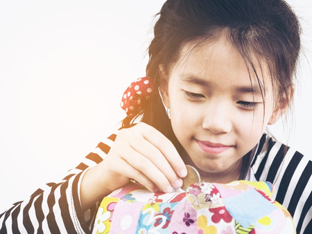 Asian kid is putting money in to a colorful piggy coin bank with calculator on wooden tableの写真素材