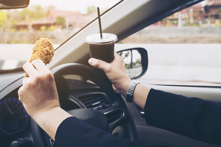 Business man driving car while eating fried chicken and cold soft drink dangerouslyの写真素材