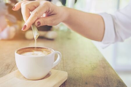 Closeup of lady pouring sugar while preparing hot coffee cupの写真素材
