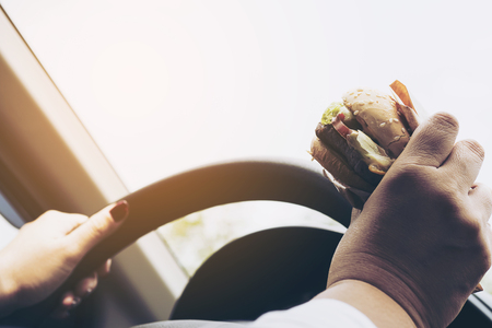 Woman driving car eating hamburgerの写真素材