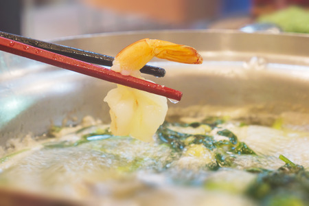 Chopsticks with shrimp in hot sukiyaki potの写真素材