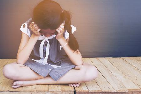Sad Asian girl sitting on white wood floorの写真素材