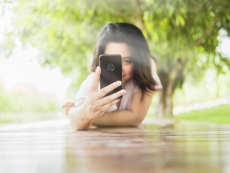 Woman lay down on wooden terrace taking photo using mobile phone in the green parkの写真素材