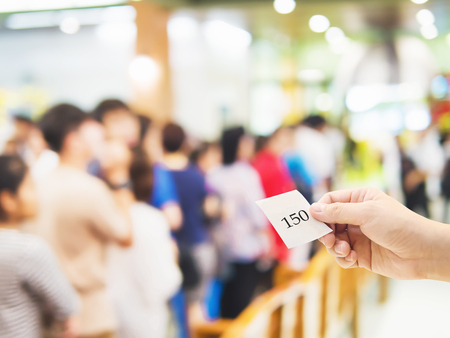 Male hand holding queue card over long line waiting people