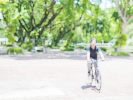 Blurred photo of bicycling buy with green tree background and white bokeh in the campusの写真素材