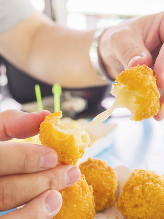 Hand is holding a stretch cheese ball ready to be eaten with soft focused french fries on blue table backgroundの写真素材