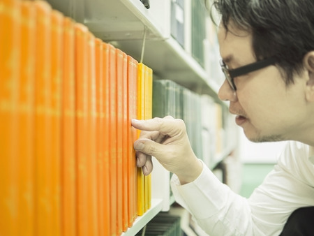 Man is selecting the book from bookshelf in a library