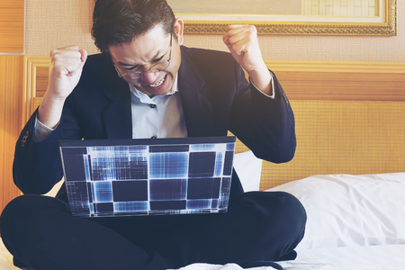Business man extremely happy while working with laptop in the hotel room during travelの写真素材