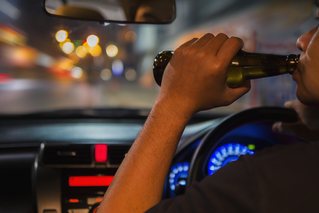Man drink beer while driving at night in the city dangerously, left hand drive systemの写真素材