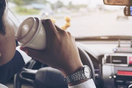 Man eating donuts with coffee while driving car - multitasking unsafe driving conceptの写真素材