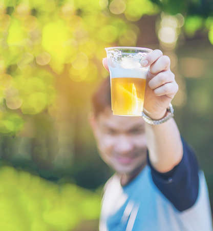 Celebration beer cheers concept - close up hand holding up glasses of beer of young man in outdoor party during his victory competition or successful task meetingの写真素材