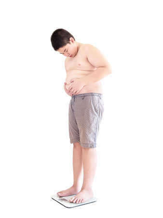 Soft focus of fat boy disappoint his fatness while standing on on weighing machine isolated over white background and included clipping path.の写真素材