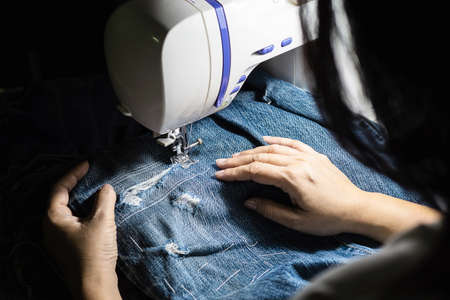 Woman doing jeans patchwork using sewing machine - home DIY sewing conceptの写真素材
