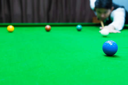 Asian man playing snooker aiming his cue stick at a white cue ball - snooker player in competition match conceptの写真素材