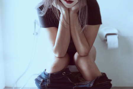 Woman sitting on toilet bowl holding tissue paper  - health problem conceptの写真素材