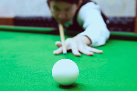 Asian man playing snooker aiming his cue stick at a white cue ball - snooker player in competition match conceptの写真素材
