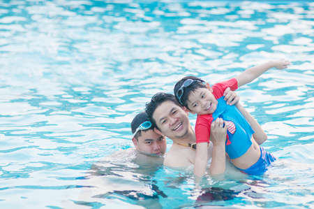Father and his two son play in clear water swimming pool - happy family play time concept